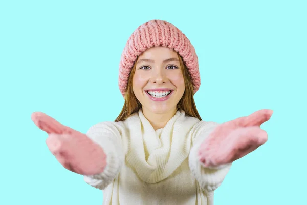 Ritratto di una giovane adolescente dai capelli rossi con un cappello rosa lavorato a maglia e guanti rosa lavorati a maglia, braccia tese verso la macchina fotografica, invitare qualcuno e sorridere su uno sfondo isolato, Capodanno — Foto Stock