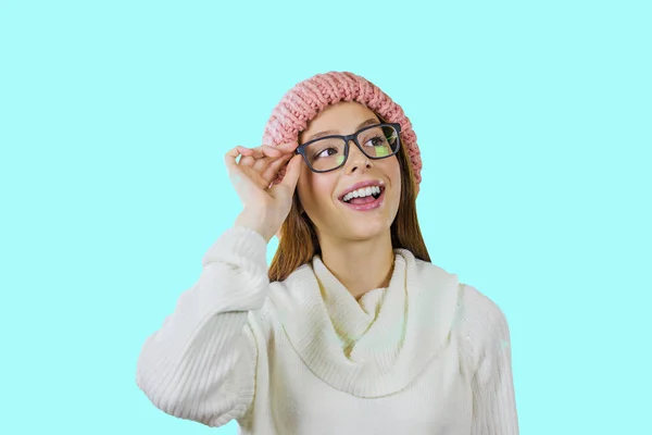 Молодая девушка с рыжими длинными волосами в розовой вязаной шляпе в очках держит очки одной рукой улыбается и смотрит в сторону вверх — стоковое фото