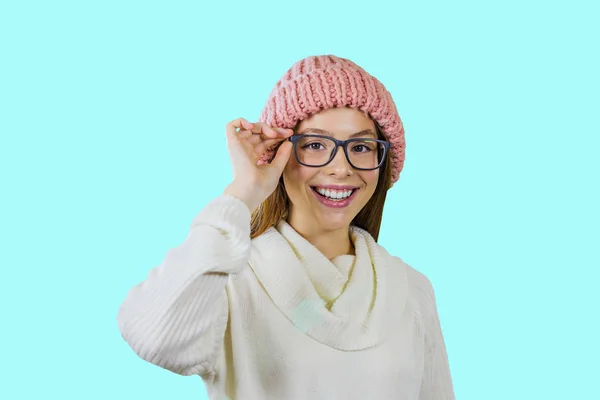 한 손으로 안경을 들고 안경을 쓰고 분홍색 니트 모자를 쓴 빨간 긴 머리를 가진 어린 소녀가 미소를 지으며 고립된 배경을 배경으로 카메라를 바라보고 있습니다. — 스톡 사진
