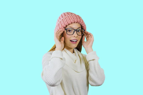 분홍색 니트 모자와 안경을 쓴 빨간 긴 머리를 한 소녀가 테두리 양쪽에 안경을 들고 미소를 지으며 고립된 배경에서 카메라를 바라보고 있습니다. — 스톡 사진