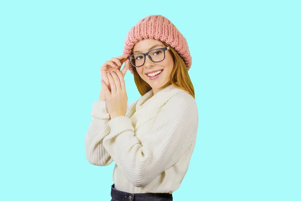 Portret van een jong roodharige meisje in een gebreide roze hoed die een bril vasthoudt met haar hand glimlachend, kijkend naar de camera tegen een geïsoleerde achtergrond, modeshow — Stockfoto