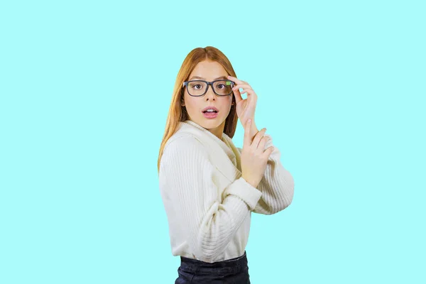Una giovane ragazza dai capelli rossi carina con gli occhiali si erge di profilo con gli occhiali sulla mano, sorpreso, sfondo isolato — Foto Stock