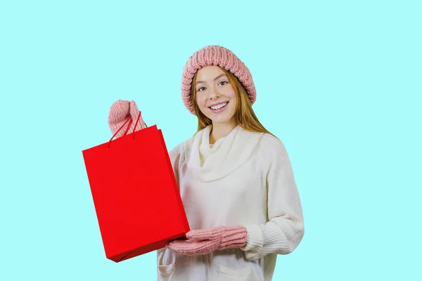 Young red-haired girl with gift bags after shopping on a blue background looking towards the camera — Stock Photo, Image