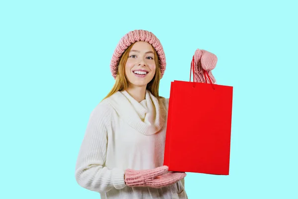 Young red-haired girl with gift bags after shopping on a blue background looking towards the camera — Stock Photo, Image