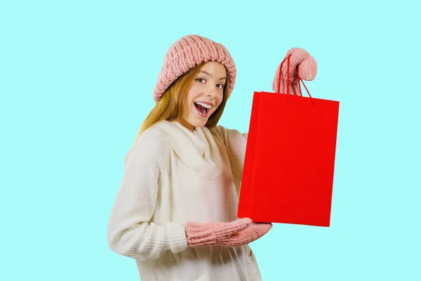 買い物の後にギフトバッグを持つ赤毛の女の子は、青い背景にカメラを見ます — ストック写真