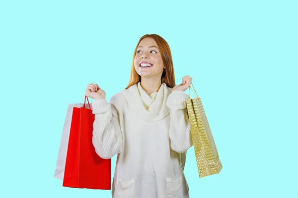 Mooi jong rood haired meisje met geschenk zakken na het winkelen op een geïsoleerde blauwe achtergrond. — Stockfoto