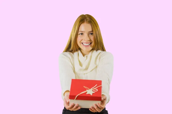Vonzó lány, hosszú vörös hajú Nézd meg a kamerát és birtokolja ajándék egy elszigetelt rózsaszín háttér — Stock Fotó