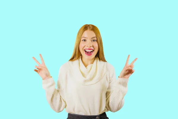 Ένα νεαρό κορίτσι με μακριά κόκκινα μαλλιά δείχνει ένα κάτουρο με τα δύο χέρια τους κρατώντας τα πάνω, χαμογελαστά με ενθουσιασμό ανοίγοντας το στόμα της στην κάμερα σε ένα απομονωμένο φόντο — Φωτογραφία Αρχείου