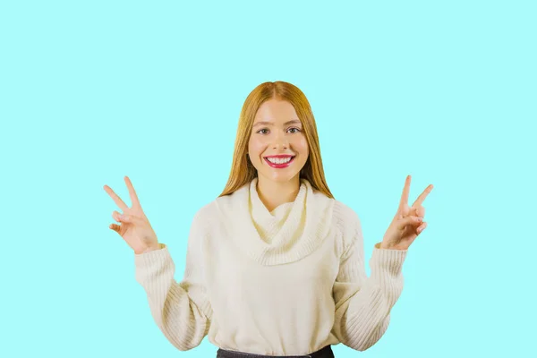 Portrait of a young girl with long red hair showing piss with both hands holding them up smiling on an isolated background — Stock Photo, Image