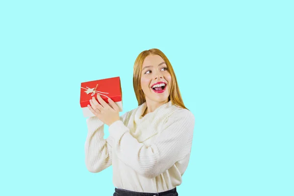 Portré egy gyönyörű vörös hajú lány, aki a gazdaság egy doboz ajándékok emelési őt szintjén arcát mosolyogva lelkesen és nézett oldalra fel egy elszigetelt háttér, a — Stock Fotó