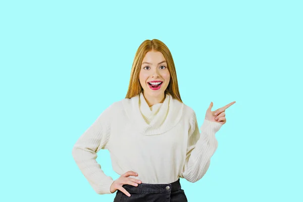 Porträt eines niedlichen rothaarigen Mädchens, das mit weit geöffnetem Mund in die Kamera lächelt, eine Hand am Gürtel hält und die zweite Hand mit dem Zeigefinger der zweiten Hand zeigt — Stockfoto