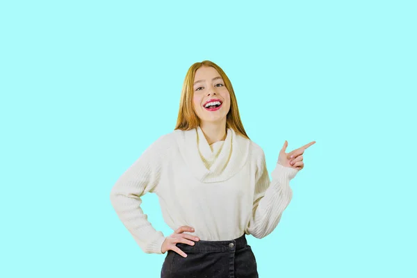 Uma menina bonita com o cabelo vermelho sorri com um sorriso, jogando a cabeça para trás e mostra com o dedo indicador no lado em um fundo isolado — Fotografia de Stock
