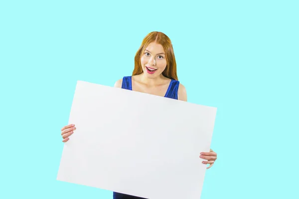 Uma jovem ruiva está segurando um grande cartaz branco ou pedaço de papel em suas mãos e está olhando para a câmera com ênfase em um fundo isolado. — Fotografia de Stock