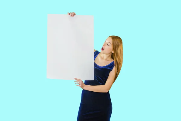 Portrait of a young red-haired girl who is holding both hands along the length of the poster looks at him with surprise and open mouth on an isolated background — Stock Photo, Image