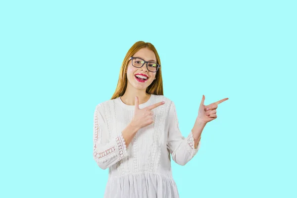 Porträt eines jungen schönen Mädchens mit langen roten Haaren und Brille, das mit den Zeigefingern beider Hände zur Seite zeigt, wie etwas demonstriert wird — Stockfoto
