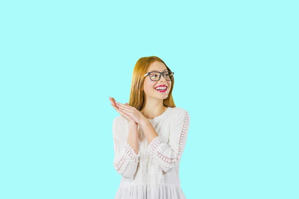 Νεαρό όμορφο κορίτσι με μακριά κόκκινα μαλλιά σε γυαλιά με διπλωμένες παλάμες μαζί χαμογελαστά αρκετά κοιτάζοντας στο πλάι, φωτογραφία σε ένα απομονωμένο φόντο — Φωτογραφία Αρχείου