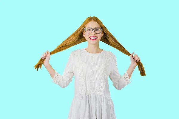 Ein rothaariges junges Mädchen mit Brille lächelt, während sie ihre Zähne zeigt und hält ihr Haar in beiden Händen, Foto auf isoliertem Hintergrund — Stockfoto