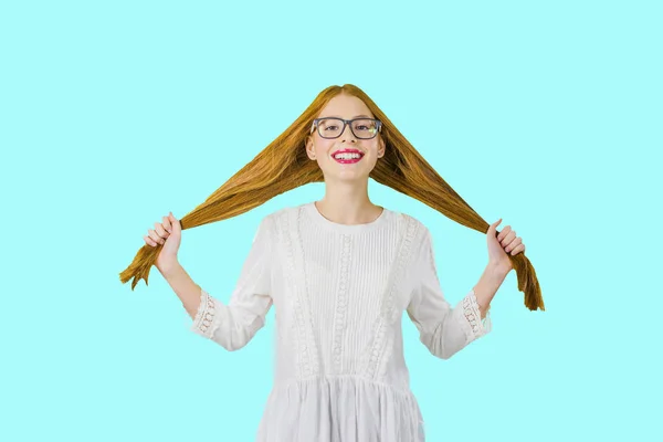 Ein rothaariges junges Mädchen mit Brille lächelt schön und hält ihr Haar in beiden Händen, Foto auf isoliertem Hintergrund — Stockfoto