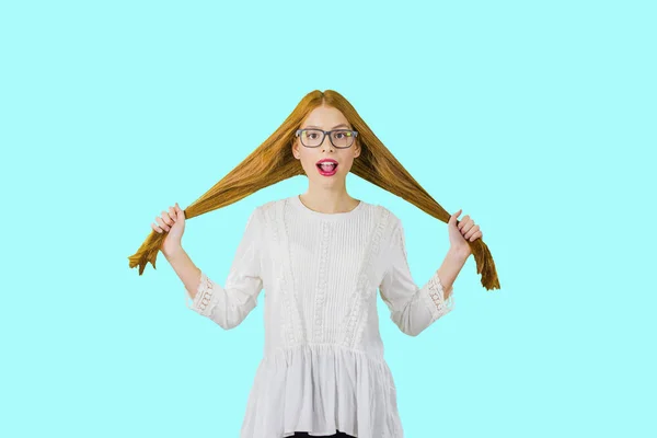 A young beautiful girl with long red hair in glasses holds her hair in both hands and expresses emotions of surprise, photo on an isolated background — Stock Photo, Image