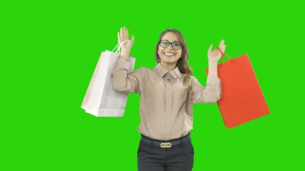 Blonde curly-haired girl in glasses holds three packages with gifts, waving them playfully and smiling on an isolated background — Stock Video