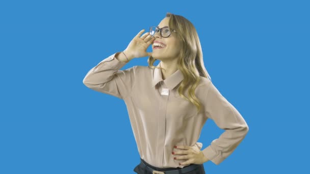Blonde girl in a satin blouse shouts or calls someone loudly and joyfully, emotions, acting on an isolated blue background — Stock Video