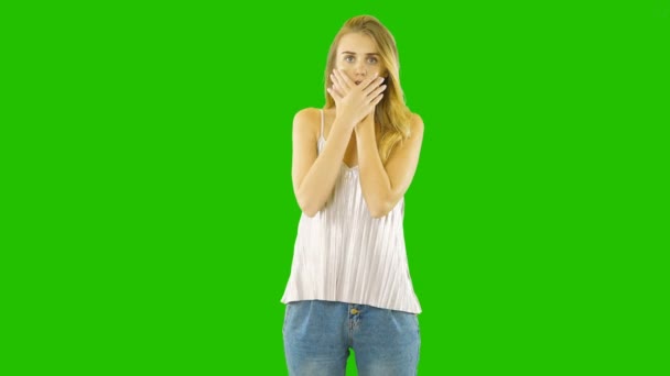 Een jonge vrouw bedekt haar gezicht met haar handen voor angst of verrassing op een groen scherm. — Stockvideo