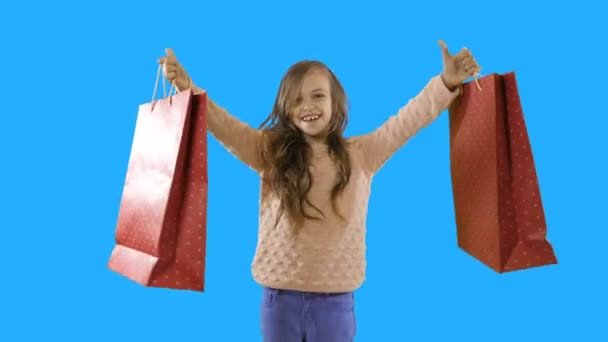 Una niña de siete años con el pelo rizado mira a la cámara sonriendo paquetes con nuevas compras o regalos, se regocija en los regalos de Año Nuevo o regalos de cumpleaños, emociones, disparos de bebés, disparos en — Vídeo de stock