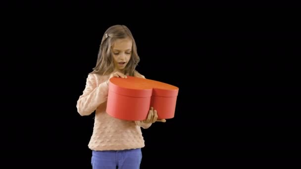 Potěšení malé holčičky, která drží červenou skříňku ve tvaru srdce v rukou, otevírá ji a radostně se usmívá a otevírá ústa dokořán, emoce, střelbu na děti, střelbu na izolované pozadí — Stock video