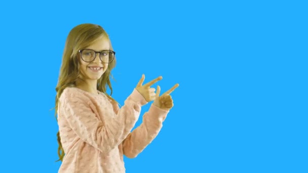 Blond meisje met krullend haar staan in profiel en shows met de wijsvingers van beide handen aan de zijkant, een demonstratie van iets, schieten op een geïsoleerde achtergrond — Stockvideo