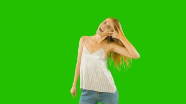 Uzun saçlı neşeli neşeli kız onu zevk gösterir. Olumlu duygular. Gözlerinin yanında iki parmağını tutarak ve yeşil bir arka plan üzerinde gülümseyerek.