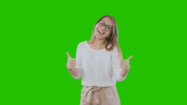 Una hermosa joven rubia en ropa de vacaciones y gafas sonríe ampliamente y muestra clase con ambas manos sobre un fondo verde . — Vídeos de Stock