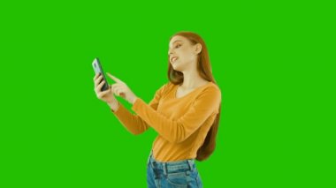 Çekici oldukça kızıl saçlı kız akıllı telefonuna bakıyor, sms yazıyor, haberleri izliyor ve olumlu duygularını gösteriyor, yeşil arka plan
