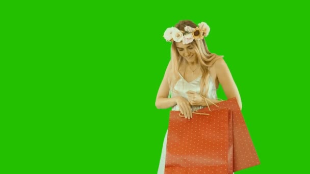 Όμορφη φακίδες κορίτσι σε ένα στεφάνι από λουλούδια κρατά πακέτα με δώρα, νέα χρόνια πακέτα, κοιτάζει στο πακέτο και χαμογελά με ενθουσιασμό, πράσινο φόντο — Αρχείο Βίντεο