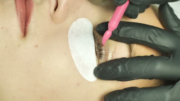 Beauty salon, eyelash extensions. Female eyes close up with selekonovoy overlay eyelid. the master of the salon with a special device applies the gel and smoothes it over the eyelashes. Eyelashes — Stock Video