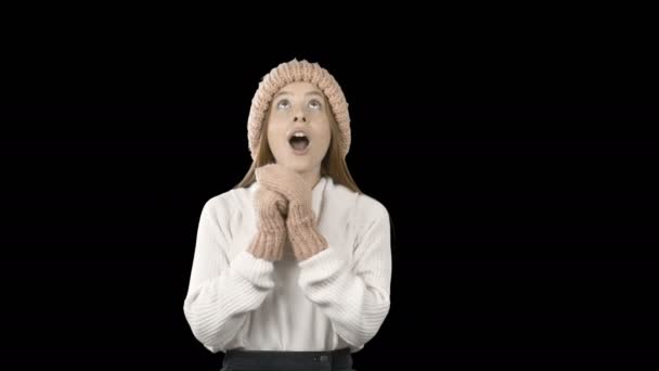 Mooi jong meisje met lang rood haar in een gebreide muts en wanten kijkt omhoog en glimlacht dan ziet er recht uit en toont klasse, schieten op een geïsoleerde achtergrond — Stockvideo