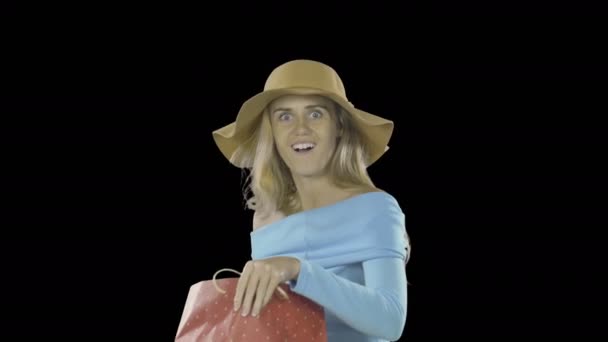 Elegant young lady with long hair and freckles on her face in a flesh-colored hat looks into the bag with a gift and smiles presses the bag to her and shows the class with both hands, shooting on an — Stock Video