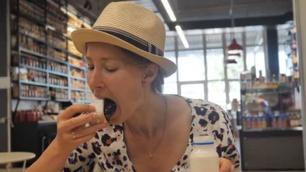 Bella ragazza affamata mangiare un dolce panino e bere yogurt in un caffè — Video Stock