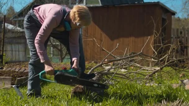 Gammal kvinna skära träd med en elektrisk såg — Stockvideo