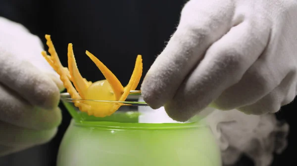 煮葡萄马丁尼鸡尾酒 用橙色的热情装饰酒保的手 玻璃杯是用蒸汽包的 — 图库照片