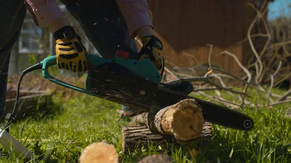 Close up woman's hands cutting tree with an electric chain saw on the courtyard of a country house. Active and healthy lifestyle concept