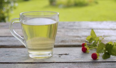 Dışarıdaki eski ahşap masaya şeffaf bir fincan çilek çayı yakın. Masada taze çiğ çilek var. Bitkisel tıp konsepti