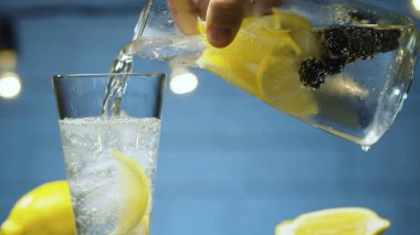 Limonatayı çiğ ve limonla bardağa doldurun. Mavi arkaplanda bulanık lambalar