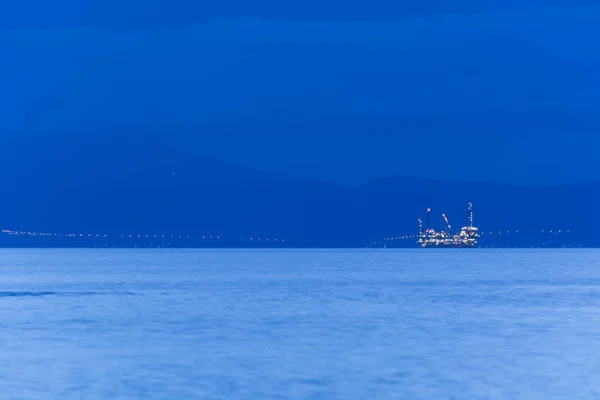 Plataforma petrolífera en alta mar al atardecer, con el continente al fondo — Foto de Stock