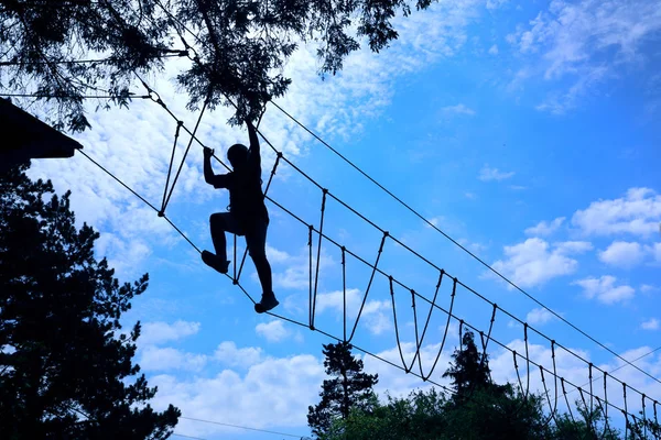 silhouette of boy climbing and taking on the challenge of a high ropes obstacle challenge course