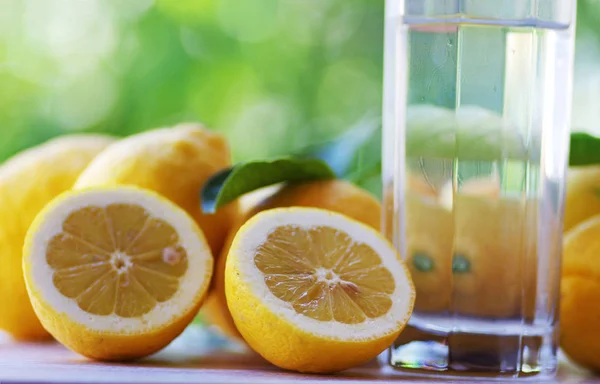 Bicchiere d'acqua e limoni gialli in tavola — Foto Stock