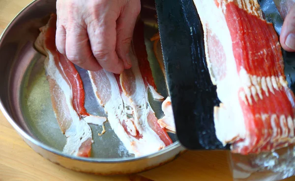 An older man prepares bacon for frying