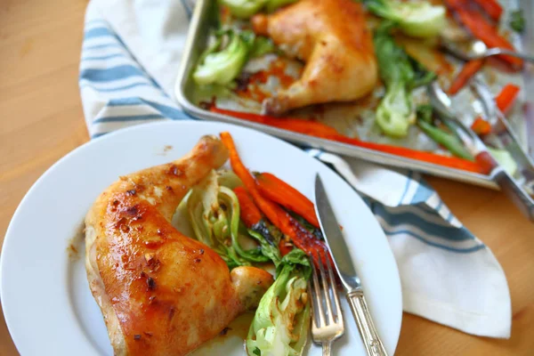 Plate with roast chicken quarter, carrots and baby bok choy with sheet pan in backgroun