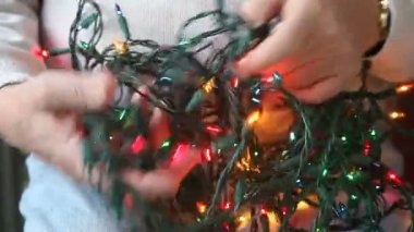 Bir adam kucağındaki Noel ışıklarını çözmeye çalışıyor.