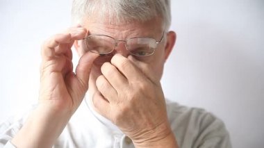 Yaşlı bir adam gözlüklerinden etkilenen bölgeyi ovuşturuyor..