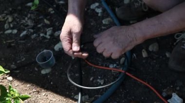 Yaşlı adam arka bahçesinde yayıcısı sulama sistemi için araç ile delik yumruklar
